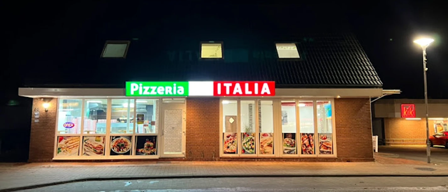Pizzaria ITALIA.jpg Die Fassade der Pizzeria ITALIA erstrahlt im Dunkeln mit leuchtenden Schildern in Rot und Grün.