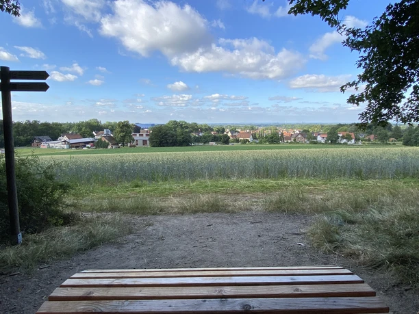 Ein Holztisch im Vordergrund bietet einen Panoramablick auf ein Dorf hinter weitläufigen Feldern.