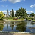 Westliches Paderquellgebiet Grüne Parklandschaft mit Fluss und Blick auf historische Gebäude bei blauem Himmel in Paderborn.