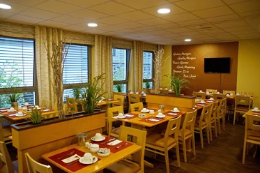 Frühstücksraum im Hotel Alberga in Mettmann Heller Frühstücksraum mit Holzmöbeln, eingedeckt für Gäste, bietet Ausblick durch große Fenster.