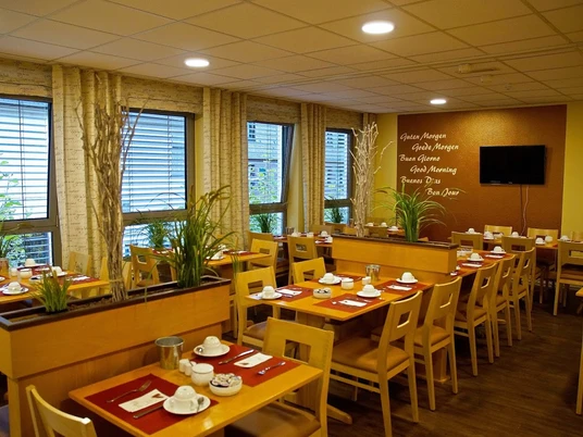 Frühstücksraum im Hotel Alberga in Mettmann Heller Frühstücksraum mit Holzmöbeln, eingedeckt für Gäste, bietet Ausblick durch große Fenster.