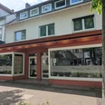 Pizzeria La Perla.jpg Zu sehen ist die Außenansicht der Pizzeria, deren Fassade in Rotbraun und Weiß gehalten ist. Die großen Fenster laden zu einem gemütlichen Mittagessen ein.