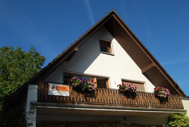 Ferienwohnung mit Holzverzierungen und blühendem Balkon vor strahlend blauem Himmel in Velbert.