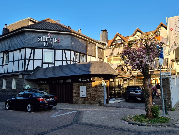 Außenansicht des Stüttgens Hotels in Velbert Fachwerk-Hotelgebäude in Velbert. Autos parken vor dem Eingang, daneben ein blühender Kirschbaum.