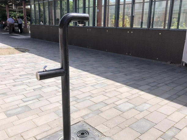 A modern, minimalist metal drinking fountain stands on a paved platform.