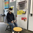 VR-Erlebnis im Zeittunnel Wülfrath Ein*e Besucher*in sitzt mit VR-Brille und Controller in einem Ausstellungsraum im Zeittunnel Wülfrath.
