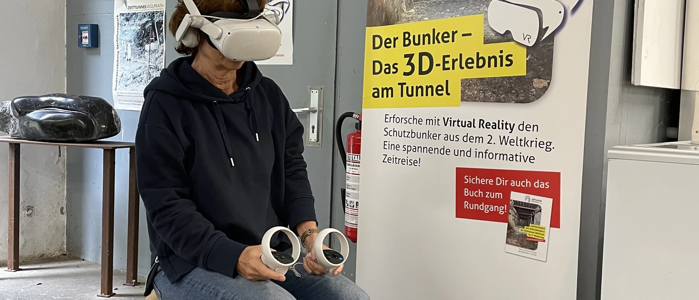 VR-Erlebnis im Zeittunnel Wülfrath Ein*e Besucher*in sitzt mit VR-Brille und Controller in einem Ausstellungsraum im Zeittunnel Wülfrath.