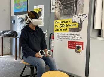VR-Erlebnis im Zeittunnel Wülfrath Ein*e Besucher*in sitzt mit VR-Brille und Controller in einem Ausstellungsraum im Zeittunnel Wülfrath.