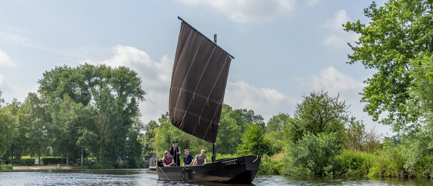 Mit dem Torfkahn auf Hamme A traditional peat boat carrying four people is sailing on the Hamme, surrounded by green river scenery.