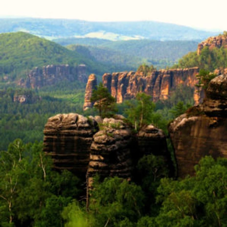 aussicht-schrammsteingratweg-2-300x300.jpg Felsformationen der Schrammsteine mit üppigem Wald im Hintergrund bei Sonnenlicht.