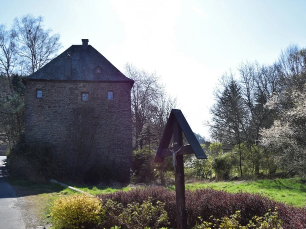Burghaus Volperhausen Altes Steinhaus in ländlicher Umgebung, umgeben von Bäumen und einem Weg, mit klarem Himmel im Hintergrund.
