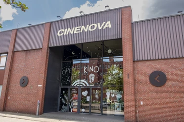 Cinenova Das Kino Cinenova befindet sich in einem roten Backsteingebäude mit einer modernen Glasfront, verziert mit kunstvollen Illustrationen.