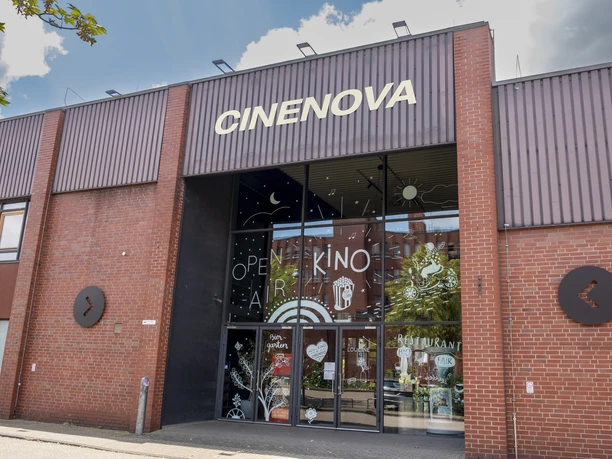 Cinenova Das Kino Cinenova befindet sich in einem roten Backsteingebäude mit einer modernen Glasfront, verziert mit kunstvollen Illustrationen.