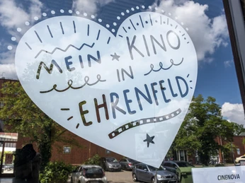 Cinenova Herzförmiger Aufkleber auf einer Glasfront mit der Aufschrift 'Mein Kino in Ehrenfeld' in lebhaften Schriftarten und Grafiken.Heart-shaped sticker on a glass front with the inscription 'Mein Kino in Ehrenfeld' in vivid fonts and graphics.