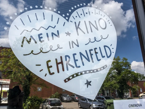 Cinenova Herzförmiger Aufkleber auf einer Glasfront mit der Aufschrift 'Mein Kino in Ehrenfeld' in lebhaften Schriftarten und Grafiken.