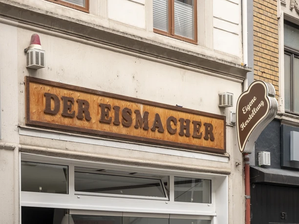 Der Eismacher Inviting entrance of a modern ice cream parlor with stylish wooden signage in an urban setting.