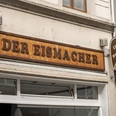 Der Eismacher Fassade eines Geschäfts mit dem Holzschild „Der Eismacher“ über der Eingangstür.Façade of a store with the wooden sign "Der Eismacher" above the entrance door.