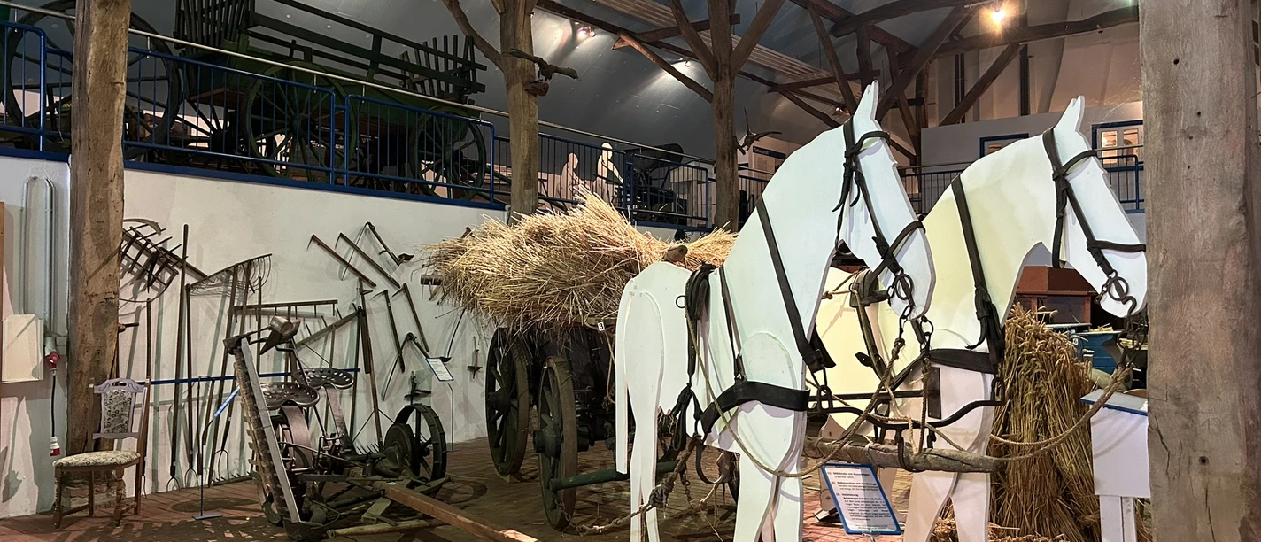 Landwirtschaftsmuseum Rhede (Ems) Ausstellungsraum mit historischen landwirtschaftlichen Geräten und Holzpferden vor einem Heuwagen