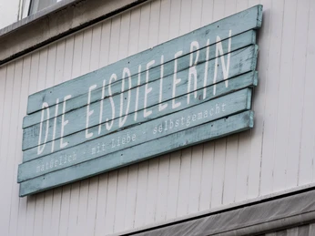Die Eisdielerin Ein Schild aus einzelnen Holzbrettern in blau gestrichen mit der Aufschrift "die Eisdielerin".A sign made of individual wooden boards painted blue with the inscription “the ice-cream seller”.