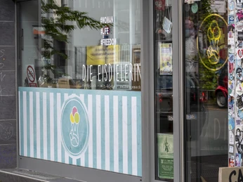Die Eisdielerin Glasfront vom Eiscafe mit urbanem Flair durch bunte Sticker an der Hauswand.Ice cream parlor with urban flair thanks to colorful stickers on the glass front.