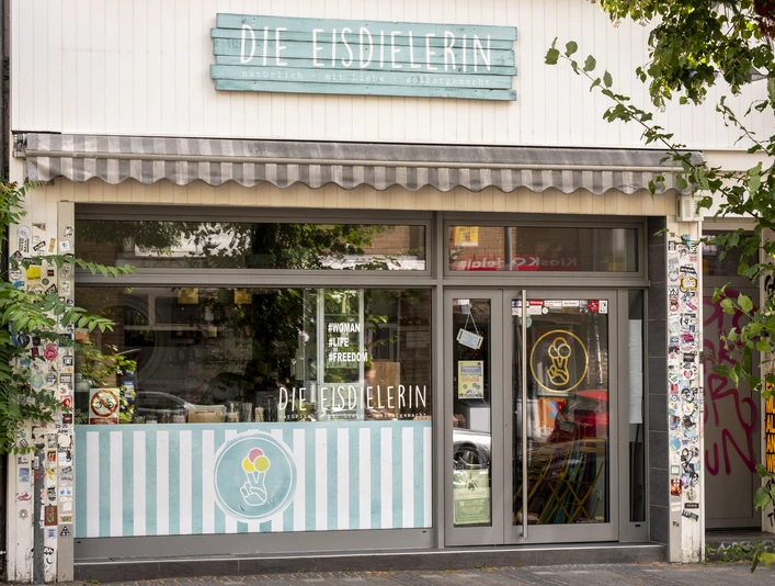 Die Eisdielerin Fröhliche beige Fassade mit hell blauem Schild aus Holzbrettern .Cheerful beige facade with a light blue sign made of wooden boards.