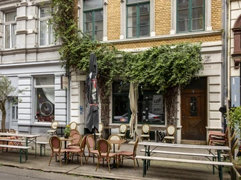 Epicerie Boucherie Außengastronomie vor einer Altbaufassade, die bewachsen ist mit grünen Blättern.Outdoor dining in front of a historic building facade covered with green leaves.