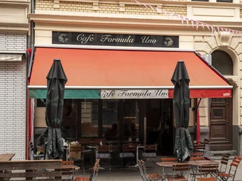 Formula Uno Außengastronomie vor einer Altbaufassade. Eine Markise ist ausgefahren und eine Wimpelgirlande flattert im Wind.Outdoor dining in front of an old building. An awning is extended and a pennant garland flutters in the wind.
