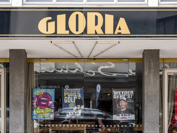 Gloria Schwarzes Schild mit goldener Aufschrift "GLORIA" über einem Kinoeingang mit bunten Filmplakaten.