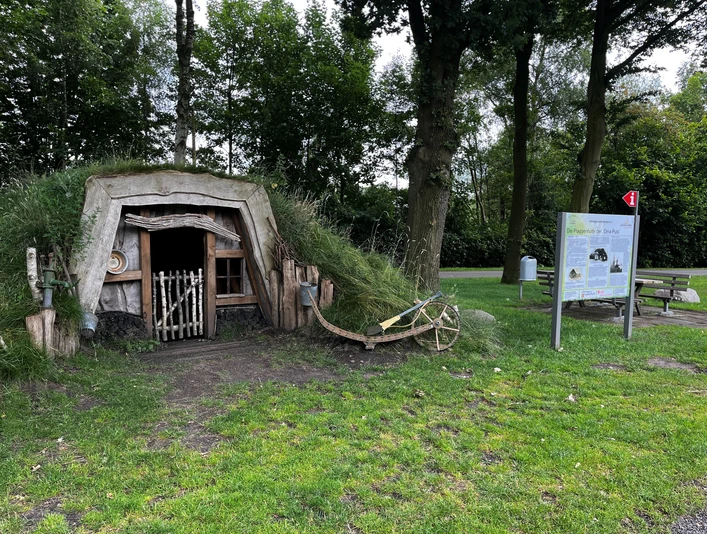 Plaggenhütte Nordloh mit Infotafel.jpg Eine traditionelle Plaggenhütte, neben einem Baum, mit Infotafel und Bank im Grünen.