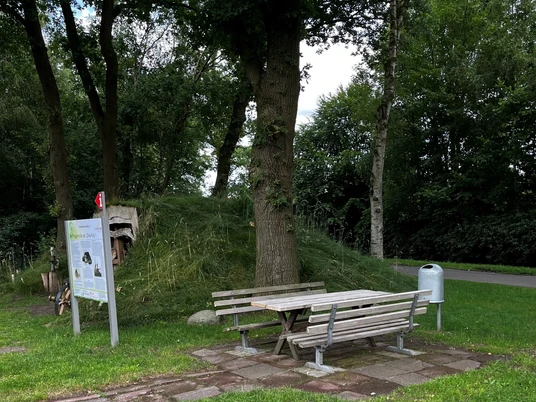 Rastplatz an der Plaggenhütte.jpg Ein ruhiger Rastplatz mit Holzbank und Tisch auf einem gepflegten Rasen, umgeben von Bäumen.