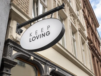 Keep Loving Stilvolle Ladenfront mit ovalem Schild "Keep Loving" und Schaufenster mit Verkaufsankündigung.Stylish store front with oval "Keep Loving" sign and shop window with sales announcement.