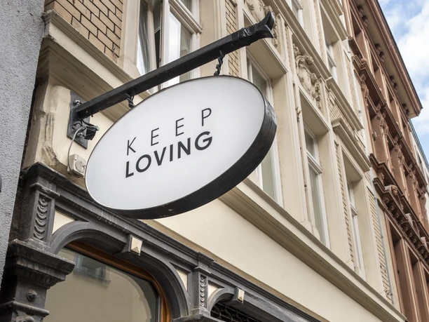 Keep Loving Stilvolle Ladenfront mit ovalem Schild "Keep Loving" und Schaufenster mit Verkaufsankündigung.