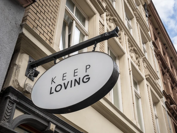 Keep Loving Ein ovales Schild mit der Aufschrift "Keep Loving" hängt an einem historischen Gebäude in der Stadt.