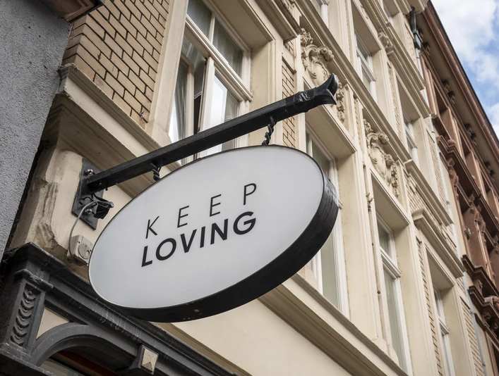 Keep Loving Ein ovales Schild mit der Aufschrift "Keep Loving" hängt an einem historischen Gebäude in der Stadt.An oval sign with the words "Keep Loving" hangs on a historic building in the city.