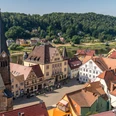 Stadt Wehlen with cyclists' church Historischer Marktplatz mit Fachwerkhäusern und einer Kirche mit Turmuhr, umgeben von grünen Hügeln und einem Fluss bei sonnigem Wetter.Stadt Wehlen with cyclists' churchMěsto Wehlen s kostelem pro cyklistyStad Wehlen met fietserskerk
