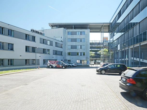 Ein modernes Bürogebäude mit einem klaren Himmel. Parkplätze sind im Vordergrund sichtbar.