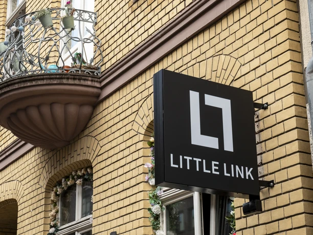 Bar Little Link The bar sign hangs in a simple design on a facade with light-colored bricks.