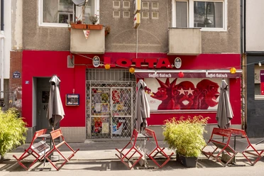 Außenansicht Fassade der Bar. Der Barbereich ist rot gestrichen und über dem Eingang hängen fünf große Buchstaben, die den Namen Lotta tragen.