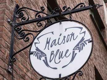 Maison Blue Restaurantschild befestigt an einer rustikal und verschnörkelten Metallhalterung.Restaurant sign attached to a rustic and ornate metal bracket.
