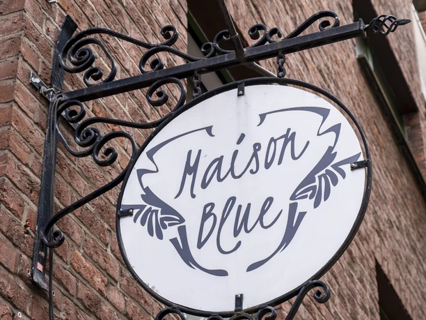 Maison Blue Restaurant sign attached to a rustic and ornate metal bracket.