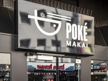 Poke Makai Die Eingangstür von Poké Makai zeigt das Logo des Restaurants und die Öffnungszeiten. Durch die Glasfront sind urbane Straßenszenen sichtbar.The entrance door of Poké Makai displays the restaurant's logo and opening hours. Urban street scenes are visible through the glass front.