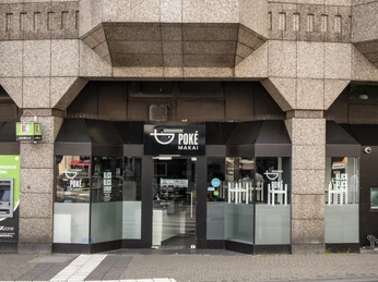 Poke Makai Außenansicht von Poke Makai im Erdgeschoss eines Gebäudes mit einer sandfarbenen Fassade und einem hohen Eingang. Oben prangt das Logo "Ernst".Exterior view of Poke Makai on the ground floor of a building with a sand-coloured façade and a high entrance. The ‘Ernst’ logo is displayed prominently above the entrance.
