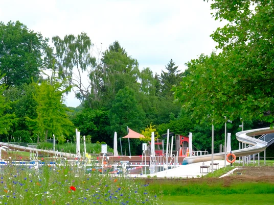 Freibad Gehlenbeck Freibad Gehlenbeck mit großer Wasserrutsche, umgeben von grünen Bäumen und bunten Blumen.