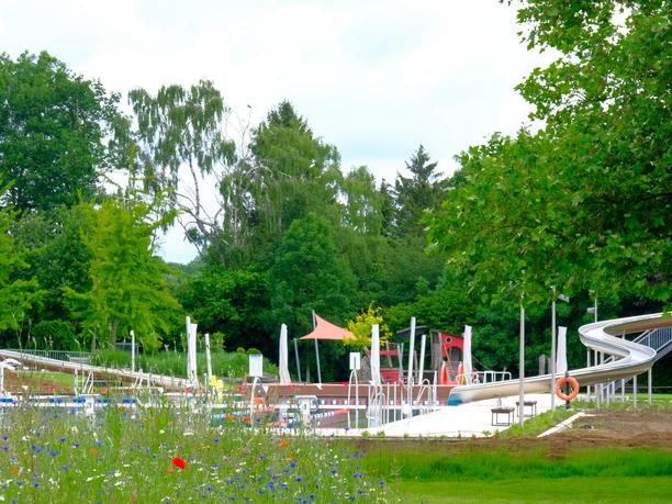 Freibad Gehlenbeck Freibad Gehlenbeck mit großer Wasserrutsche, umgeben von grünen Bäumen und bunten Blumen.