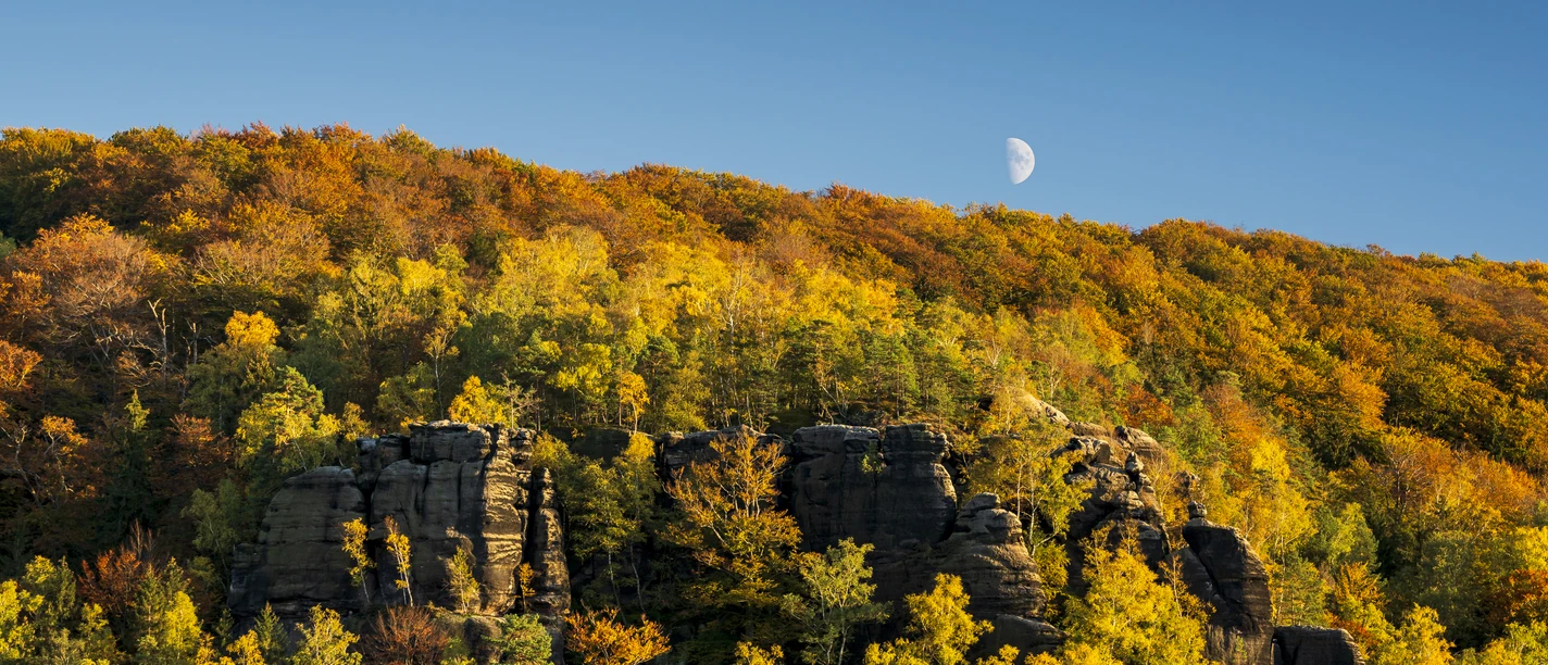 Great Winter Mountain in autumn Autumnal landscape with colorful deciduous forest and rocks in the foreground, crescent moon in the clear blue sky.