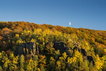 Großer Winterberg im Herbst Herbstliche Landschaft mit buntem Laubwald und Felsen im Vordergrund, Halbmond am klaren blauen Himmel.