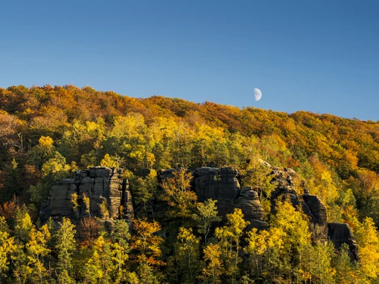 Großer Winterberg im Herbst Herbstliche Landschaft mit buntem Laubwald und Felsen im Vordergrund, Halbmond am klaren blauen Himmel.Autumnal landscape with colorful deciduous forest and rocks in the foreground, crescent moon in the clear blue sky.Podzimní krajina s barevným listnatým lesem a skalami v popředí, půlměsíc na jasně modré obloze.Jesienny krajobraz z kolorowym lasem liściastym i skałami na pierwszym planie, półksiężyc na czystym, błękitnym niebie.Herfstlandschap met kleurrijk loofbos en rotsen op de voorgrond, maansikkel in de helderblauwe lucht.Paesaggio autunnale con foresta di latifoglie colorate e rocce in primo piano, luna crescente nel cielo azzurro.