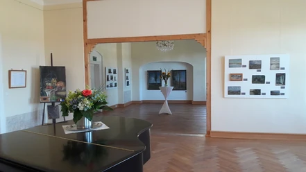 A bright showroom with a wooden floor, paintings on the walls, a flower arrangement on a table and a chandelier on the ceiling.