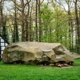 Großer Stein Tonnenheide Naturdenkmal Großer Stein in Tonnenheide vor Fachwerkhaus, umgeben von dichten, grünen Bäumen.