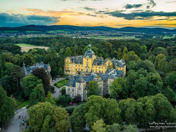 Schloss Bückeburg Luftaufnahme von Schloss Bückeburg, umgeben von üppigen Bäumen, Feldern und einem bewölkten Himmel.